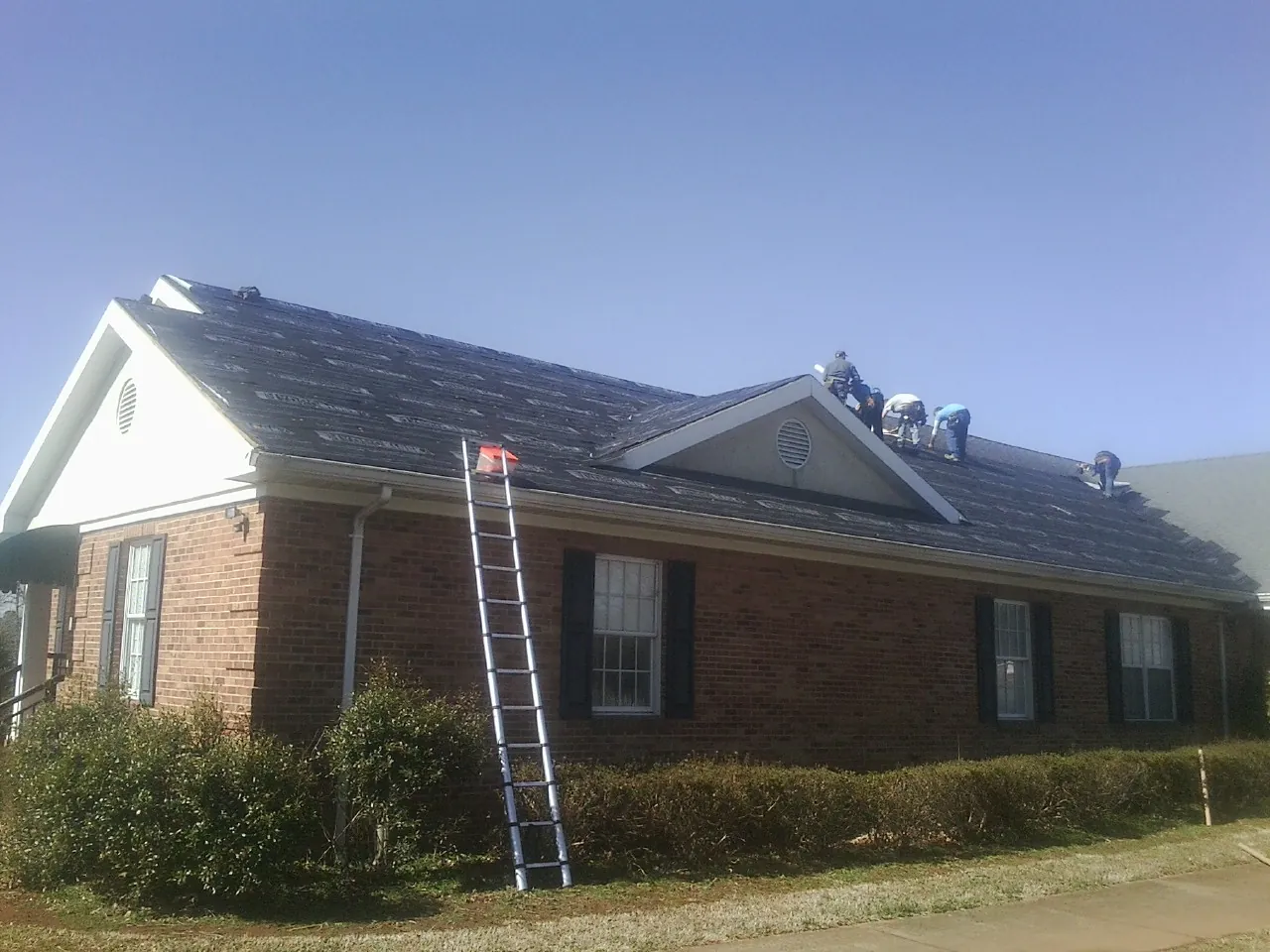 Crew tearing shingles off a brick ranch roof with a ladder set — Emergency Roof Repair work by our crew in Kirkwood