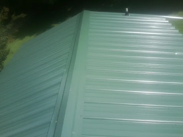 New green metal panels meeting at the ridge of a roof — Flat Roof Repair work by our crew in Kirkwood